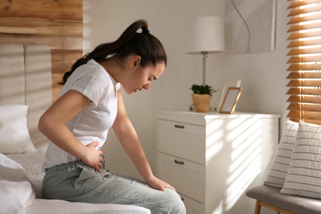 Frau sitzt mit Darmschmerzen im Bett