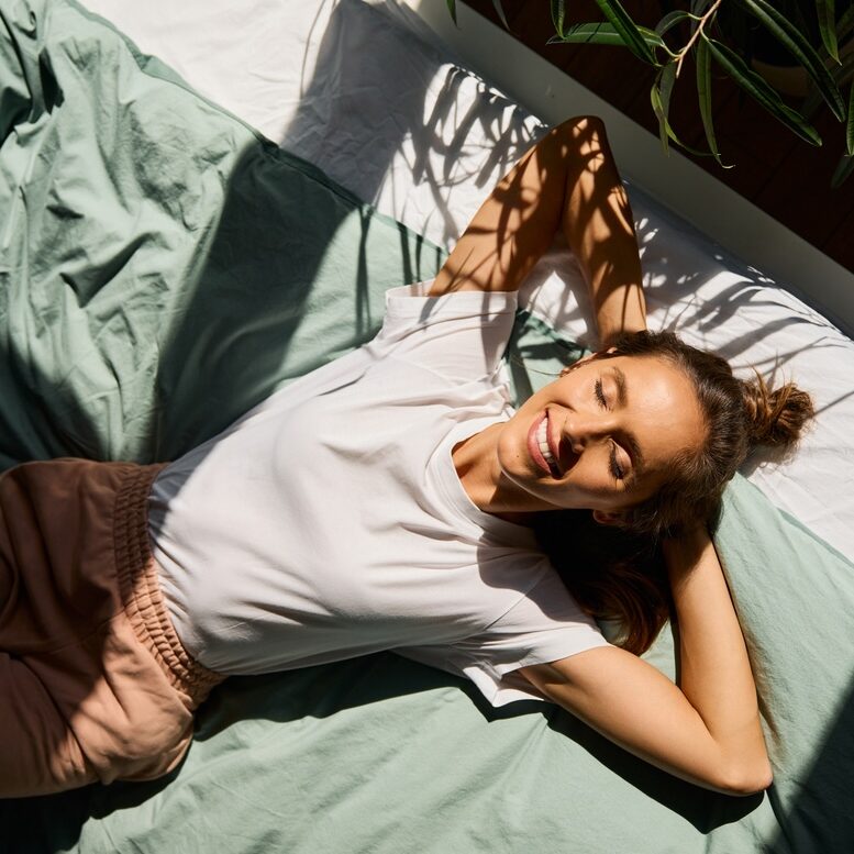 Gesunde Frau liegt im Bett und l&auml;chelt, gut gelaunt, scheint fit und aktiv zu sein.